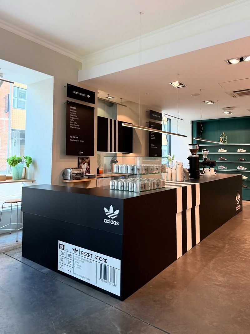 The Friends & Family Kiosk inside Rezet Store: a black counter with white adidas stripes, menu boards and walls of sneakers behind it.