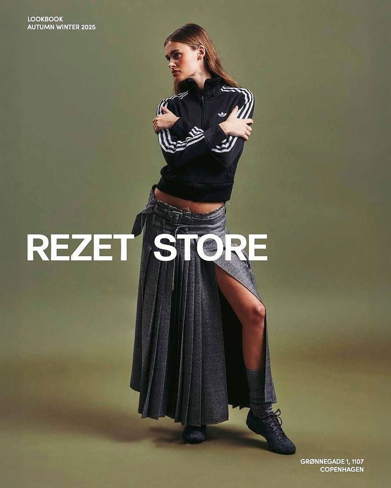 Cover of the Rezet Store Lookbook Autumn Winter 2025: a model in a black track jacket and a long grey skirt against an olive background.